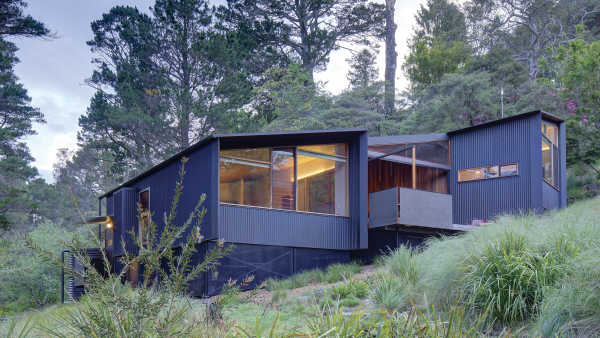 Blue-gray house sits on a forested slope 