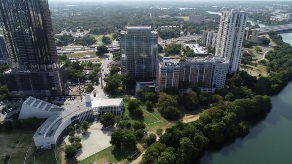 Drone shot of a section of downtown Austin with Lady Bird Lake and buildings in the forefront, Interstate-35 in the background