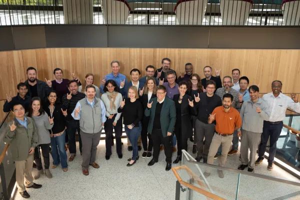 A group of faculty smiling and looking up at the camera with their hands in the "hook em" symbol