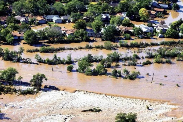 Flood waters flowing through the Dove Springs neighborhood. Only the tops of houses and trees are above the brown waters.