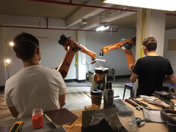 Two students seen from behind watching the KUKA robotic arm in action