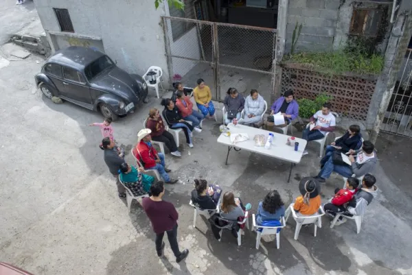 Overhead shot of a group of people sitting in plastic lawn chairs around a table in the streets of Monterrey
