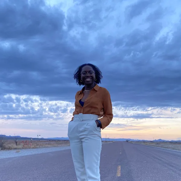 Temi Osanyintolu with her hands in her pockets smiling at the camera, standing in the middle of the road in West Texas, with the sunset in the background