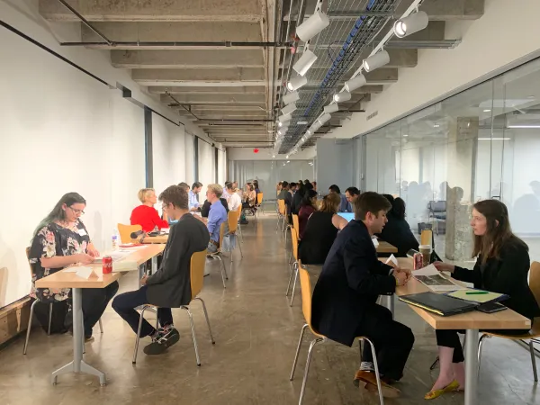 Students sitting across tables from employers in a well-lit and welcoming hallway in the WMB