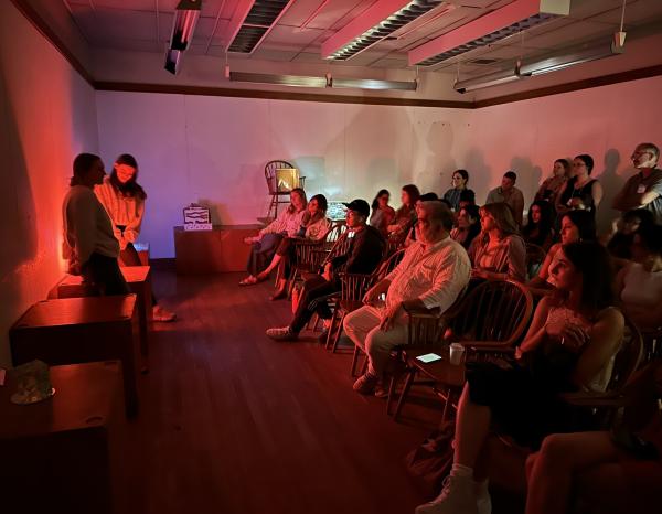 Interior design students gather in a dark red-lit room with Jorge Pardo to display their illuminated creations