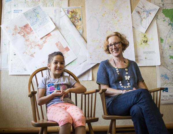 Liz Mueller sitting in front of a wall of maps and papers with a child in the chair next to her