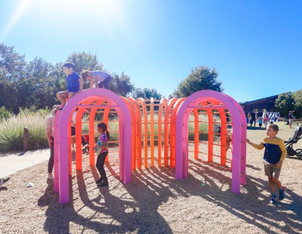 Several children climbing on and interacting with a vibrantly colored set of arches at the Wildflower Center's Fortlandia