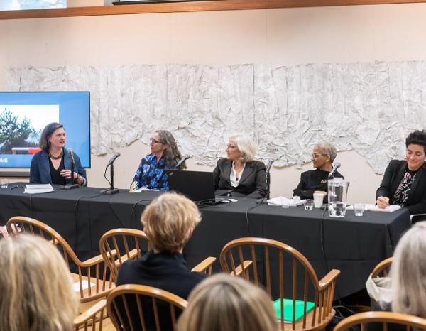 Several women sit on a panel in front of an audience