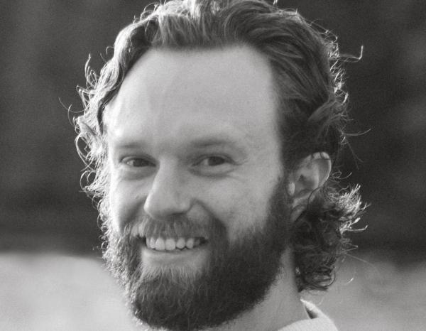 A bearded man smiling at the camera in black and white