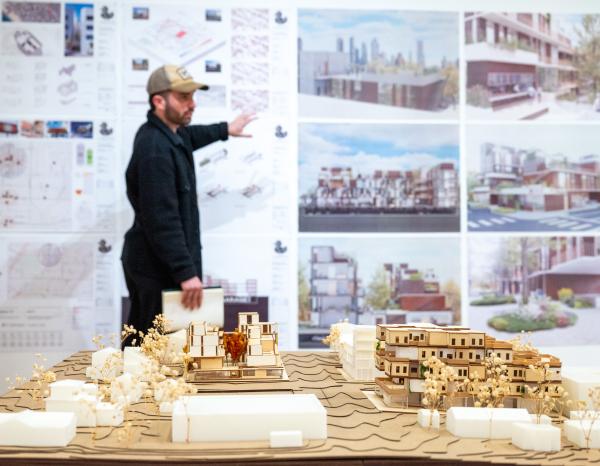 A student presenting work during final reviews with a large architecture model in the foreground.