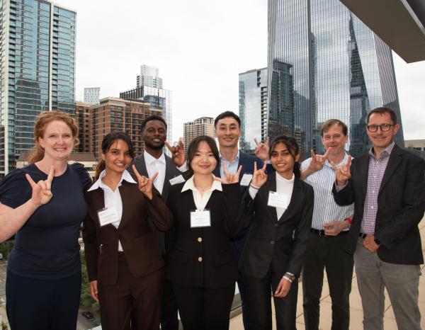 Five students pose with three faculty members, doing a hook em horns hand sign
