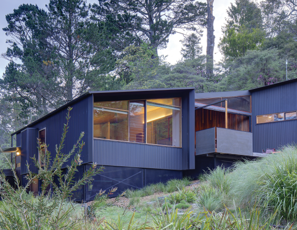 Blue-gray house sits on a forested slope 