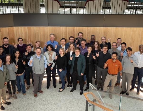 A group of faculty smiling and looking up at the camera with their hands in the "hook em" symbol