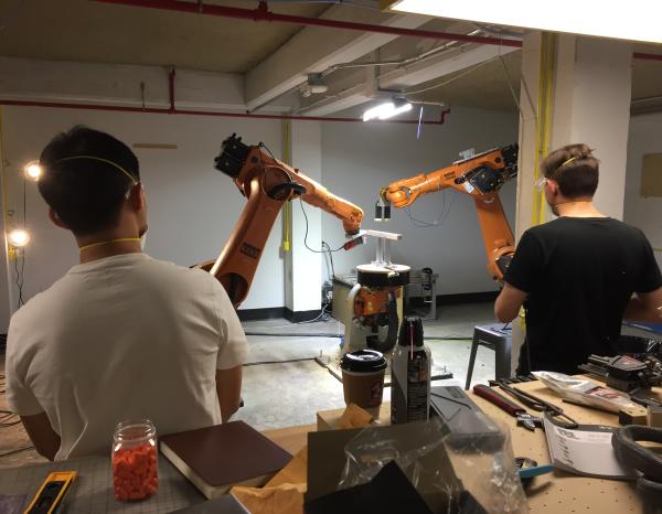 Two students seen from behind watching the KUKA robotic arm in action