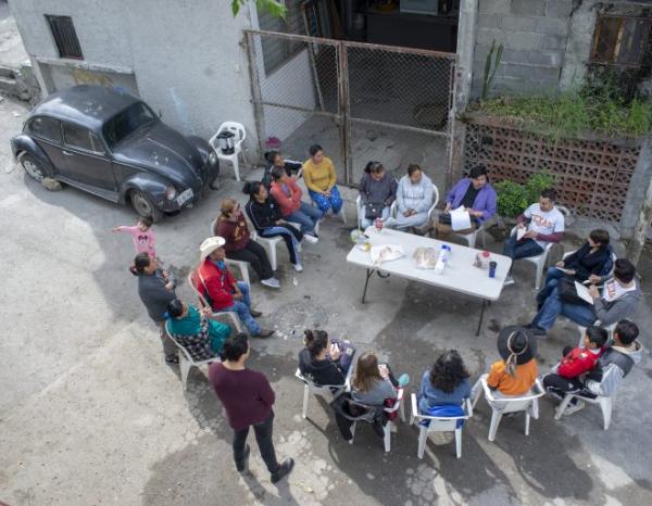 Overhead shot of a group of people sitting in plastic lawn chairs around a table in the streets of Monterrey