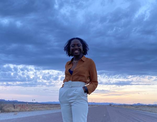 Temi Osanyintolu with her hands in her pockets smiling at the camera, standing in the middle of the road in West Texas, with the sunset in the background