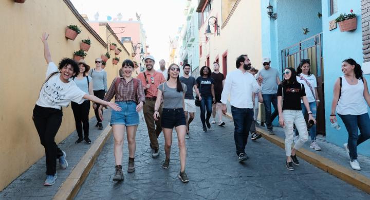 A group of students walking outside in a colorful alleyway in Mexico, smiling and interacting with each other