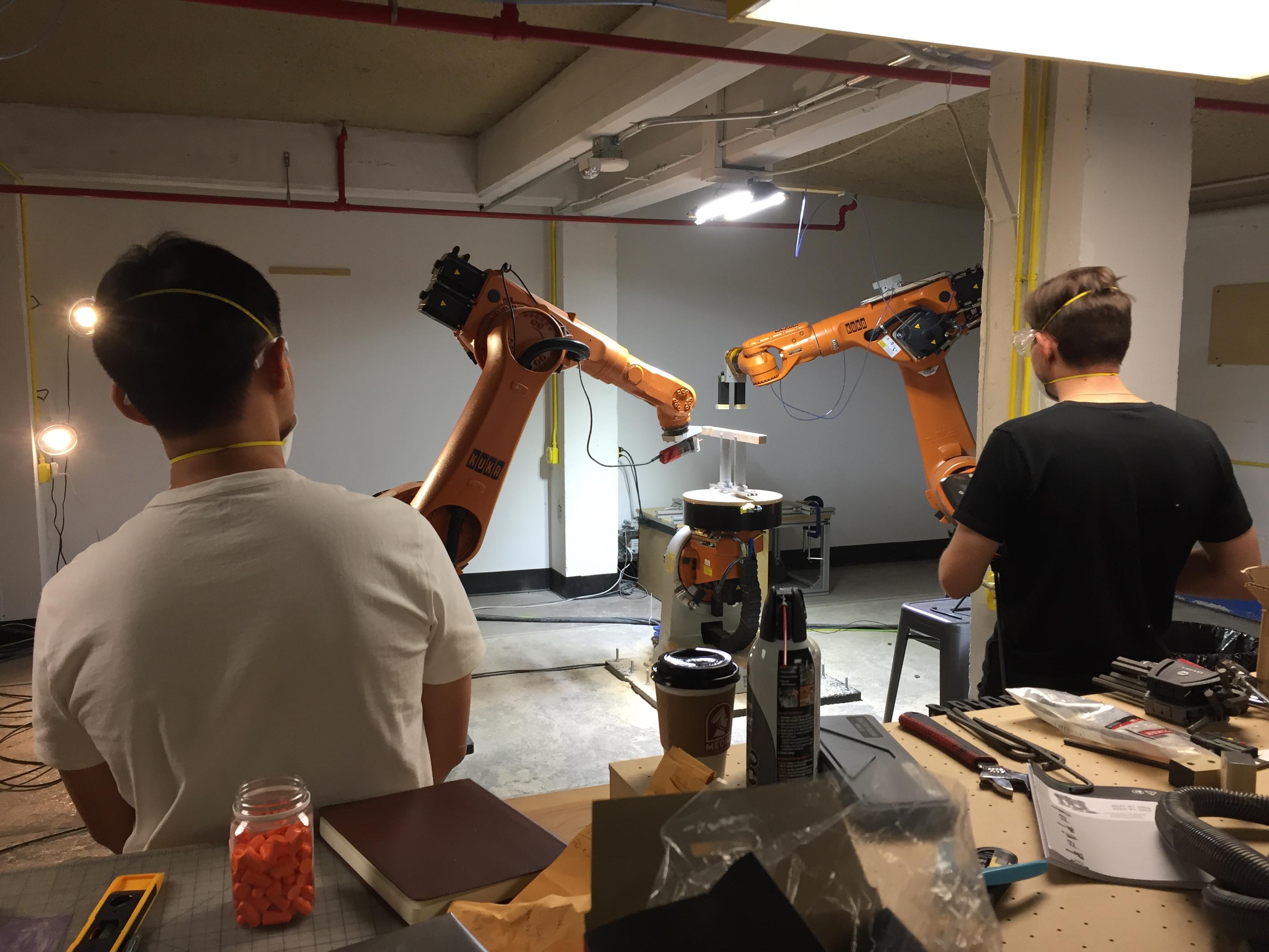 Students seen from behind, looking at a robotic arm in the Technology Lab.