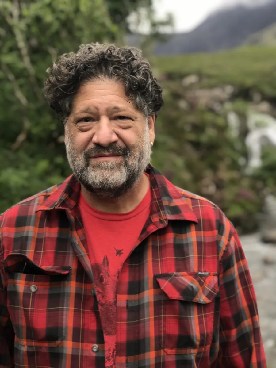 Rich Heyman wearing a red undershirt and a red flannel stands in front of a green, natural setting