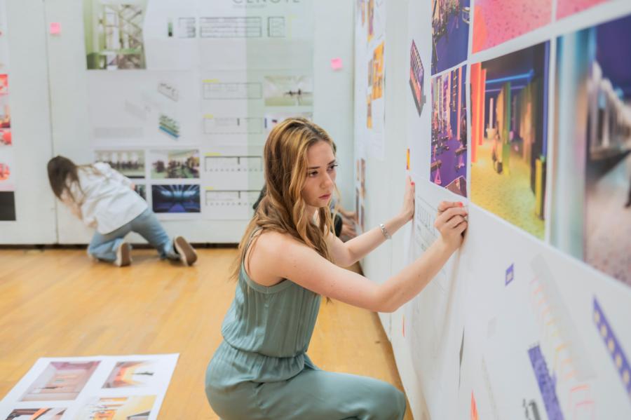 A female student pins her work up during final reviews.