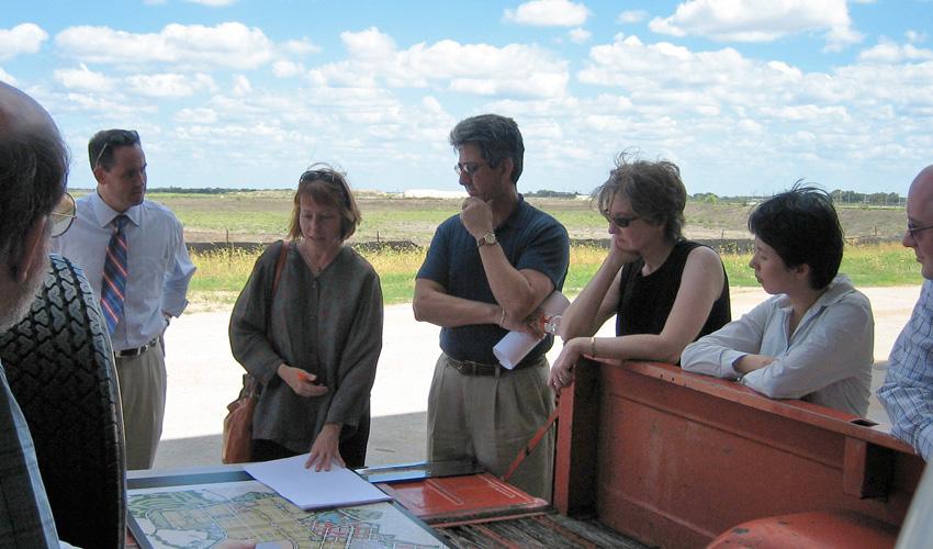 Group of people in discussion, standing in a circle around a map.