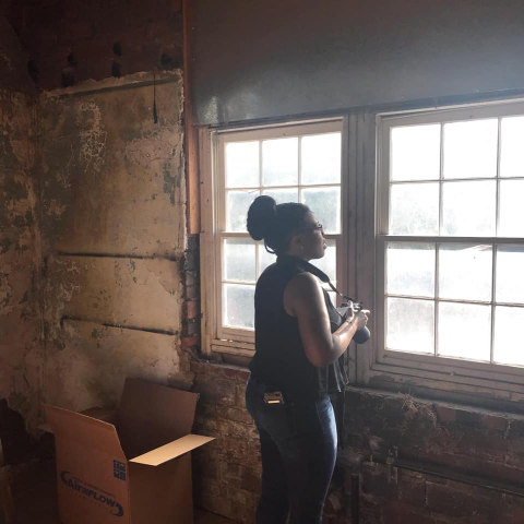 Tara Dudley holds a camera while looking out a window.