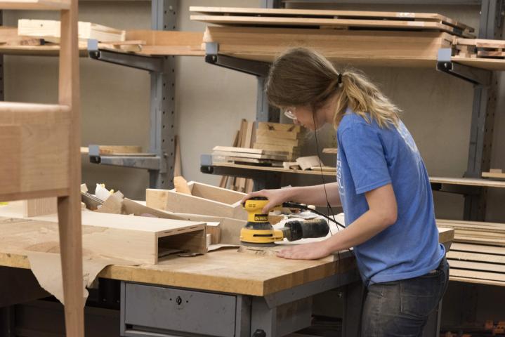A student seen sanding a piece of wood in the Build Lab