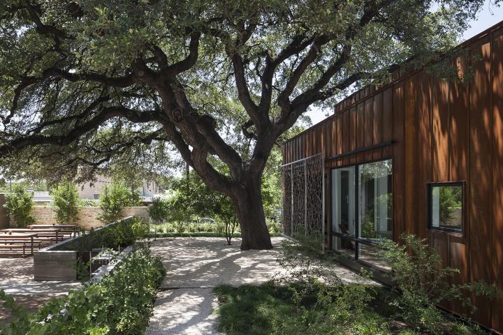 Exterior shot of a red-toned, wood paneled home with a large shade tree out front