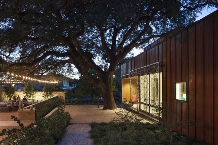 Exterior shot of a home at night with a large shade tree and twinkle lights illuminating the patio on the far left where people are seen sitting around a table