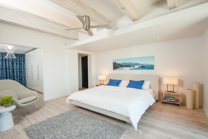 A bedroom with light wood floors and a white bed with blue pillows