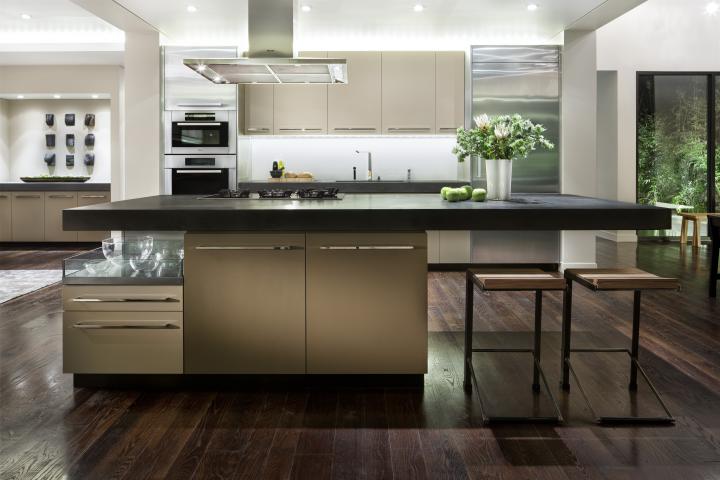 A shot of a kitchen space with an island with negative space in the forefront, an oven range and lighter wood cabinets.