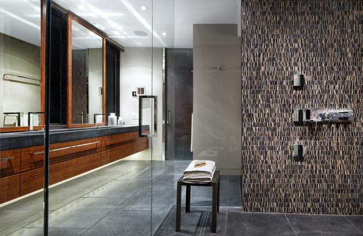 An interior shot of a bathroom with a brown, textured tile wall, and a wood vanity