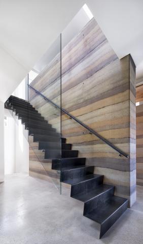 A modern black staircase against a layered stone wall