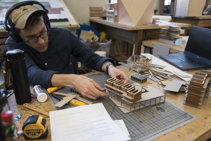 A student in a hat wearing headphones while he works in studio on a model