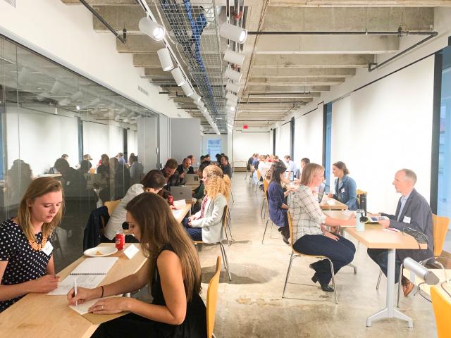 Two rows of tables are set up in a long hallway as students sit across from employers who are looking over their portfolios as part of Career Services' Portfolio Workshop.