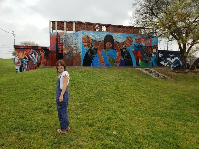 Student standing in a green field in front of a mural