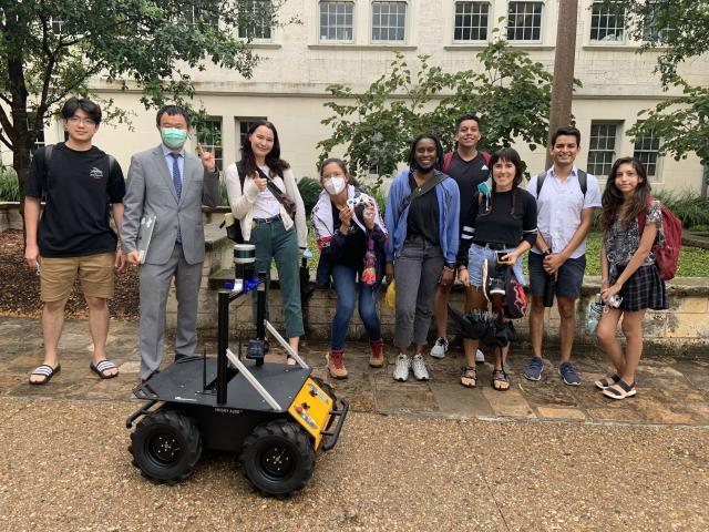 Students and Junfeng Jiao stand behind a robot outside the School of Architecture