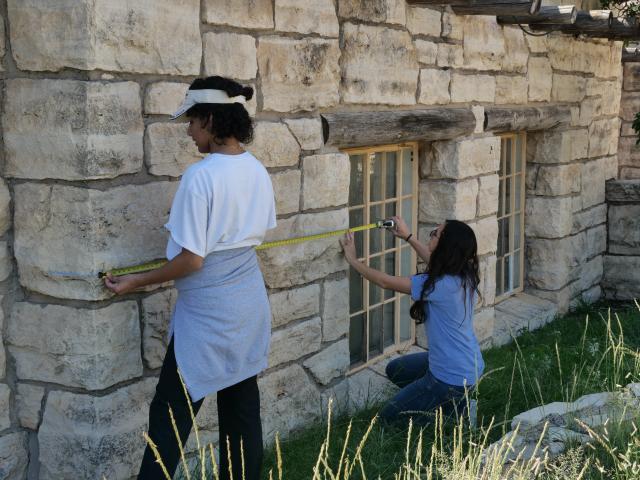 Two students measuring the exterior of a historic stone building