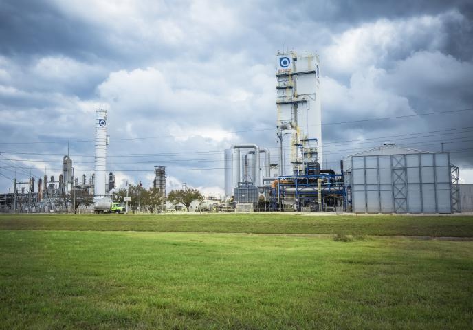 A factory on a cloudy day with a green field in the foreground.